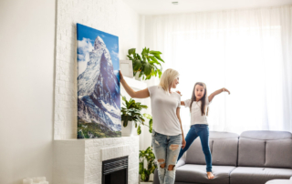 Woman and daughter hanging painting in brightly-lit room.