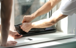 Two men apply window tint to a window in a home.